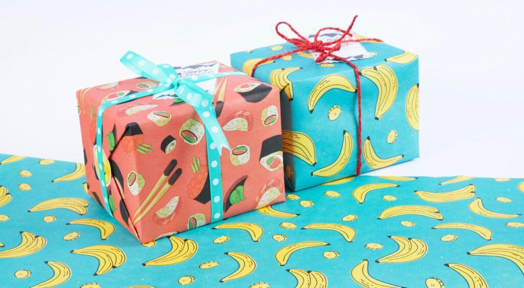 Amazon verpackt auch Geschenke! Zwei Geschenke verpackt in jeweils rotes und blaues Papier mit Sushi- und Bananen-Print