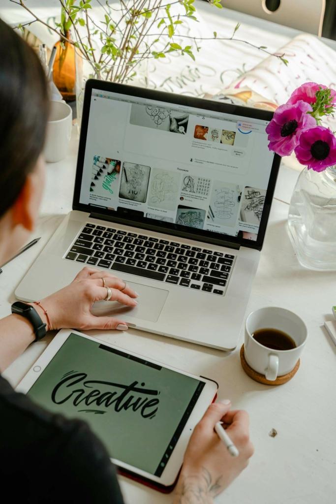 Overhead view of a workspace with a person working on a design labeled "Creative" on a tablet, with a laptop and a cup of coffee nearby.