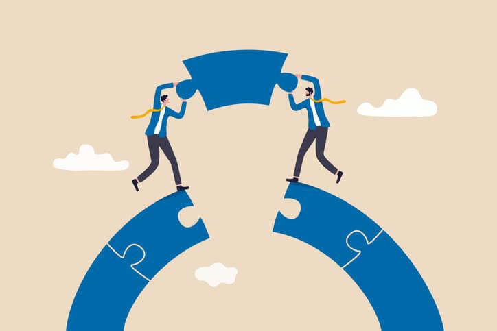 An illustration of two businessmen standing on top of a round puzzle and holding the missing piece together, suggesting the development of a SaaS partnership strategy.