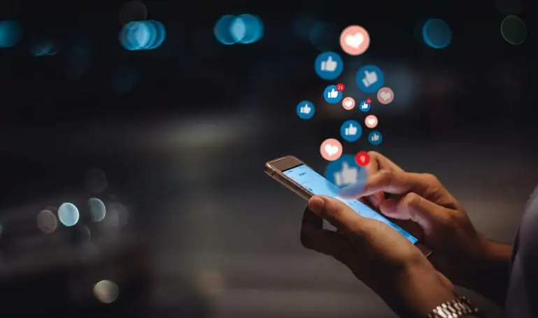 Close-up of a person using a smartphone with floating social media icons of likes, hearts, and reactions, symbolizing social media engagement and interaction.